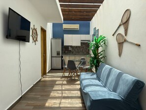 Ein schmales Entree mit einer Couch, einem Fernseher, einer Küchenzeile und einem Esstisch.