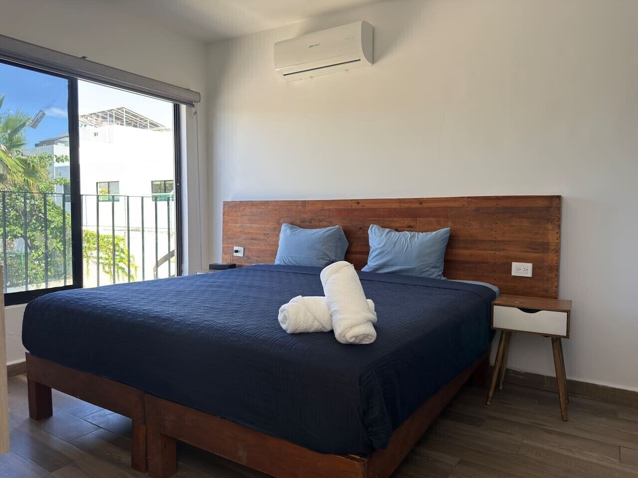 Ein Schlafzimmer mit einem großen Bett, einem hölzernen Kopfteil, zwei Kissen, einem Nachttisch und einer Klimaanlage.