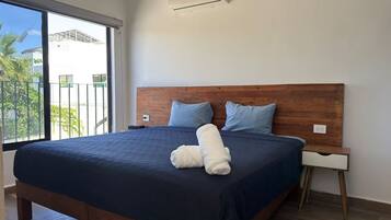 Ein Schlafzimmer mit einem großen Bett, einem hölzernen Kopfteil, zwei Kissen, einem Nachttisch und einer Klimaanlage.