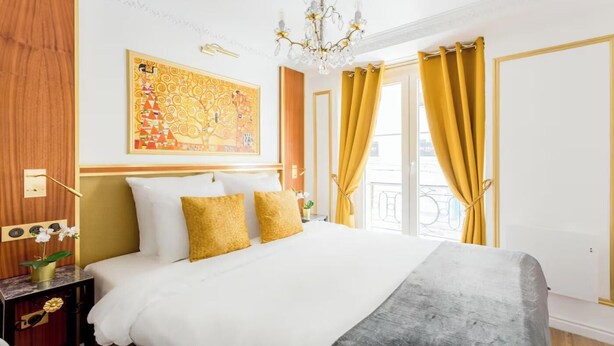 Ein Hotelzimmer mit einem großen Bett, einer Kristallleuchter, einem Gemälde und gelben Vorhängen.