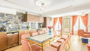 Een moderne keuken met een marmeren achterwand, een eethoek met roze stoelen en een groot raam met oranje gordijnen.