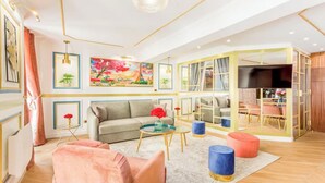 Ein modernes Wohnzimmer mit einer Couch, einem Couchtisch, einem Hocker, einem Bild an der Wand und einem Fernseher im Hintergrund.