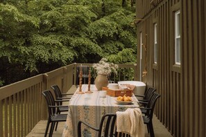 A wooden deck with a table set for dining, surrounded by chairs, and a backdrop of dense green foliage.