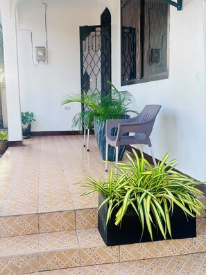 A tiled patio area with a bench, potted plants, and a wall-mounted electrical box. - Bagamoyo Residence Slow down, Breathe & Live fully (Bagamoyo)
