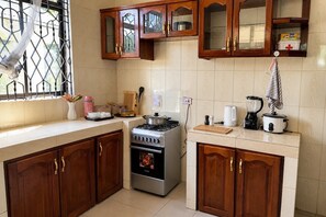 A kitchen with wooden cabinets, a stove, a blender, and a window with a decorative item.