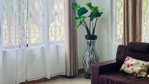 A room with a large window, a potted plant, a sofa, and a patterned vase.