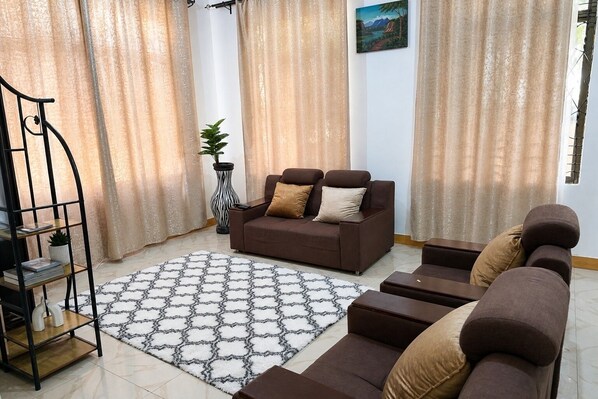 A living room with a sofa set, a patterned rug, and a decorative plant.
