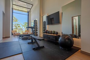 Ein modernes Fitnessstudio mit Trainingsgeräten, einem Fernseher und Blick auf Bäume.