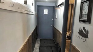 A narrow hallway with a dark door at the end, wooden paneling on the walls, and a small mat at the entrance. - ML130 Charming 1-bedroom condo in SnowShoe.  Just steps from the slopes. (Snowshoe)