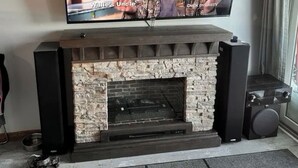 A television on a fireplace mantel with a stone surround, a speaker to the right, and a metal bowl on the floor. - ML130 Charming 1-bedroom condo in SnowShoe.  Just steps from the slopes. (Snowshoe)