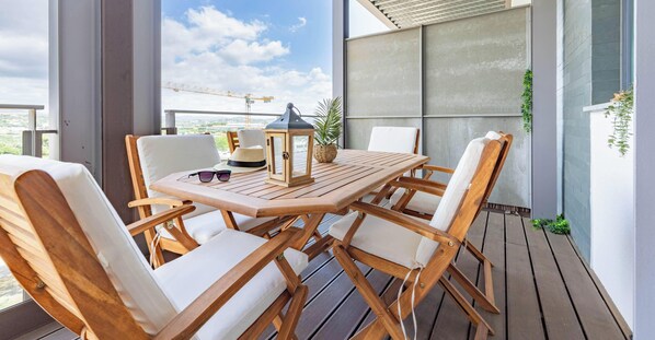 Eine Holzterrasse mit Tisch und Stühlen, einer Laterne und Blick auf die Baustelle im Hintergrund.