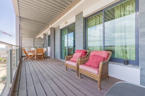 Ein Balkon mit Korbmöbeln, großen Fenstern und Blick auf die Stadt.