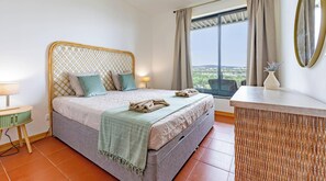 Ein Schlafzimmer mit Bett, Nachttisch, Lampe und Blick ins Freie.