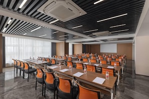 A conference room with rows of tables and chairs, a projector screen, and a large window with curtains.