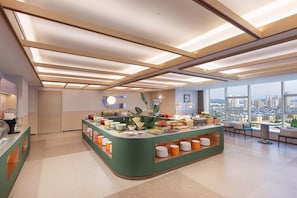 A modern hotel lobby with a central buffet, large windows, and a city view.