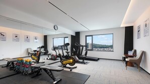 A modern gym with various exercise equipment, large windows, and a city view.