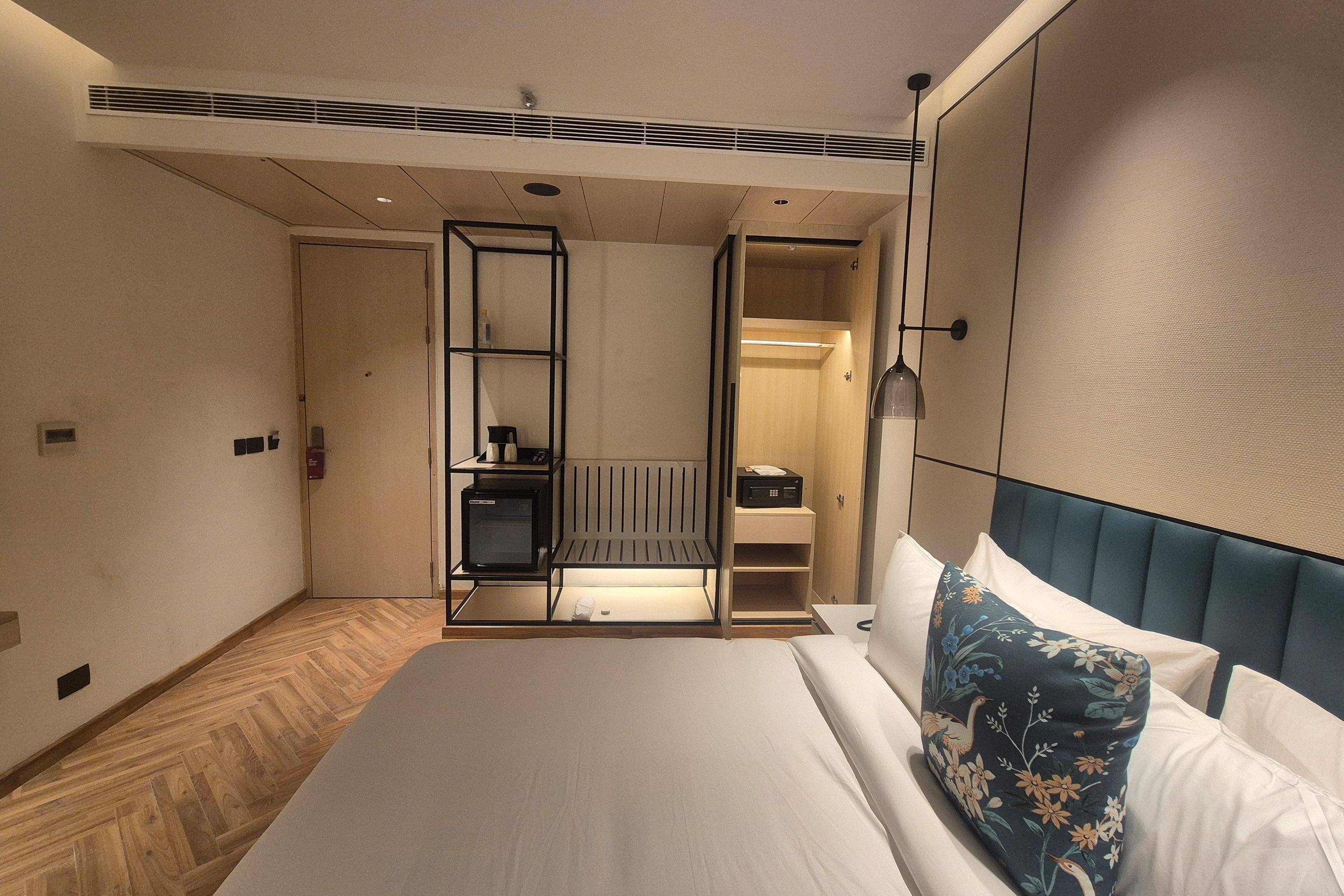 A hotel room with a bed, a bedside table, a wardrobe, and a built-in heater.