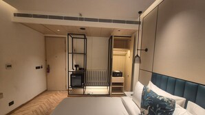 A hotel room with a bed, a bedside table, a wardrobe, and a built-in heater. - Ramada Encore by Wyndham Vrindavan Rukmani Vihar (Vrindavan)