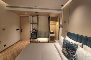 A hotel room with a bed, a bedside table, a wardrobe, and a built-in heater. - Ramada Encore by Wyndham Vrindavan Rukmani Vihar (Vrindavan)