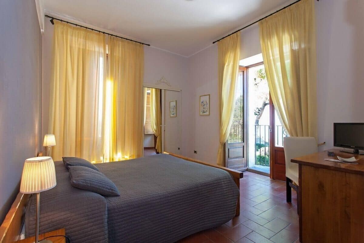 A bedroom with a bed, bedside lamp, wooden desk, and a television.