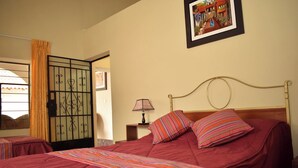 Une chambre d’hôtel avec deux lits, une fenêtre avec des rideaux, un tableau accroché au mur et une table de chevet avec une lampe.