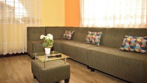 Un salon avec un canapé, un pouf et une table basse en verre.