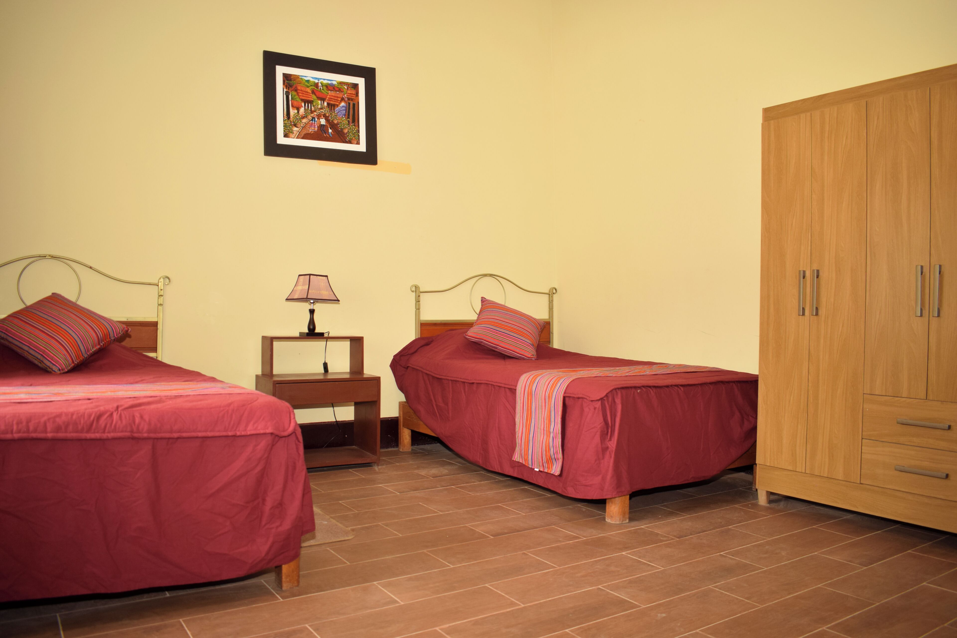 Ein Schlafzimmer mit zwei Betten, einem Nachttisch, einer Lampe, einem Kleiderschrank und einem gerahmten Bild an der Wand.