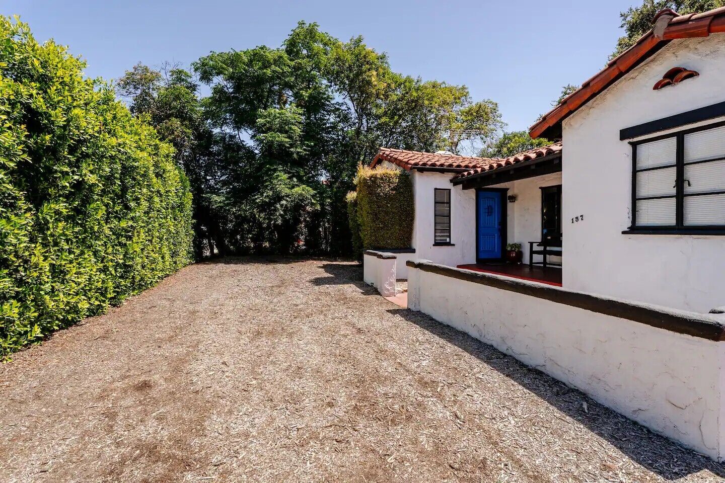 Un edifici blanc amb teules vermelles, una porta blava i un camí d'accés de grava.