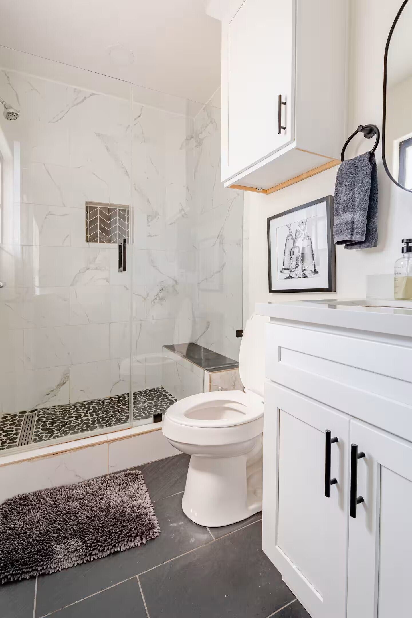 Un baño con ducha, inodoro y armarios blancos.