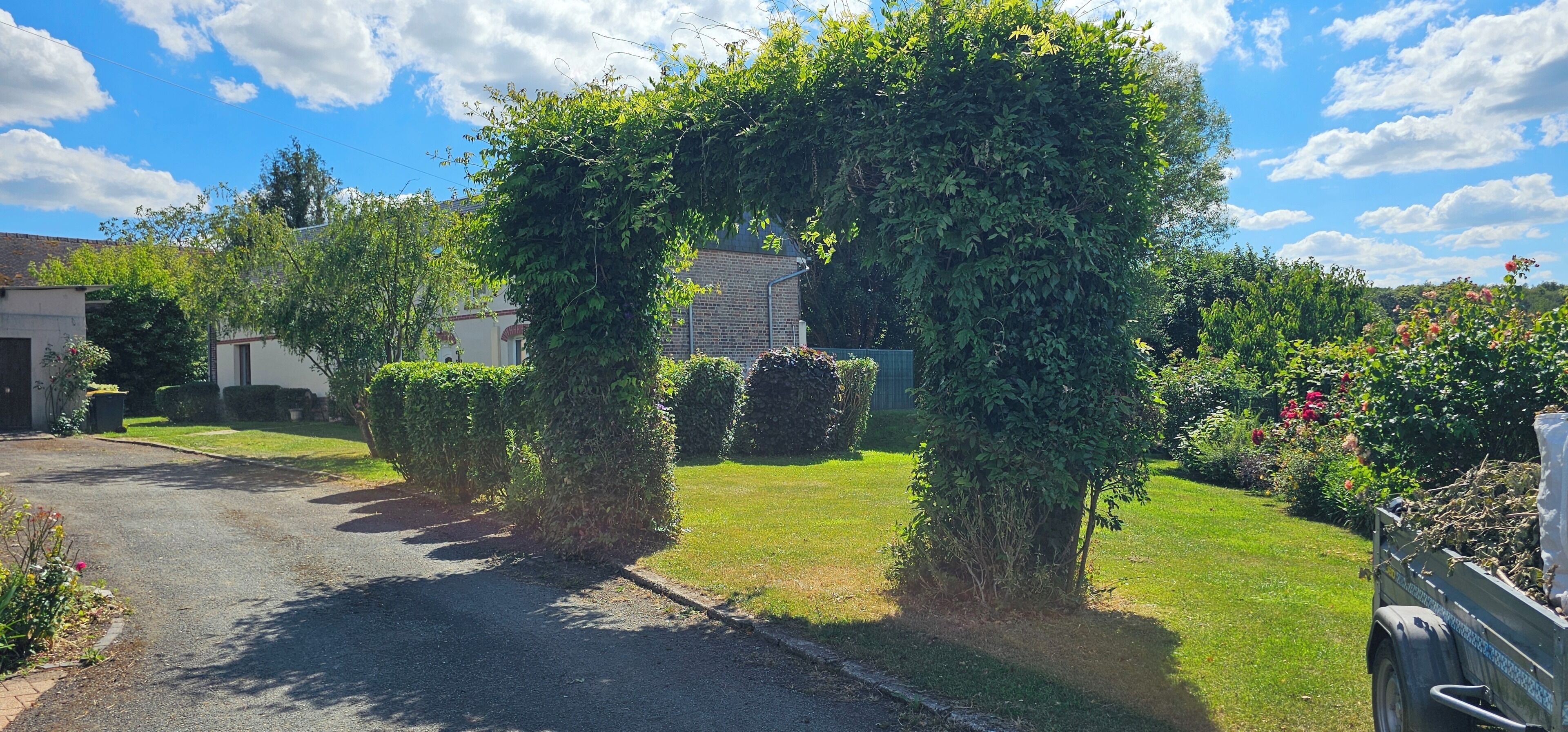 A residential street with a hedge archway, a grassy lawn, and a parked vehicle.