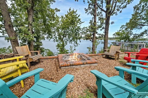 Ein Sitzbereich im Freien am Seeufer mit Adirondack-Stühlen und einer Feuerstelle.