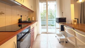 A modern kitchen with a stove, sink, and a view of the outside through a glass door. - 1BR next to Pasalimani, Marina Zeas & Hospital (Pireas)