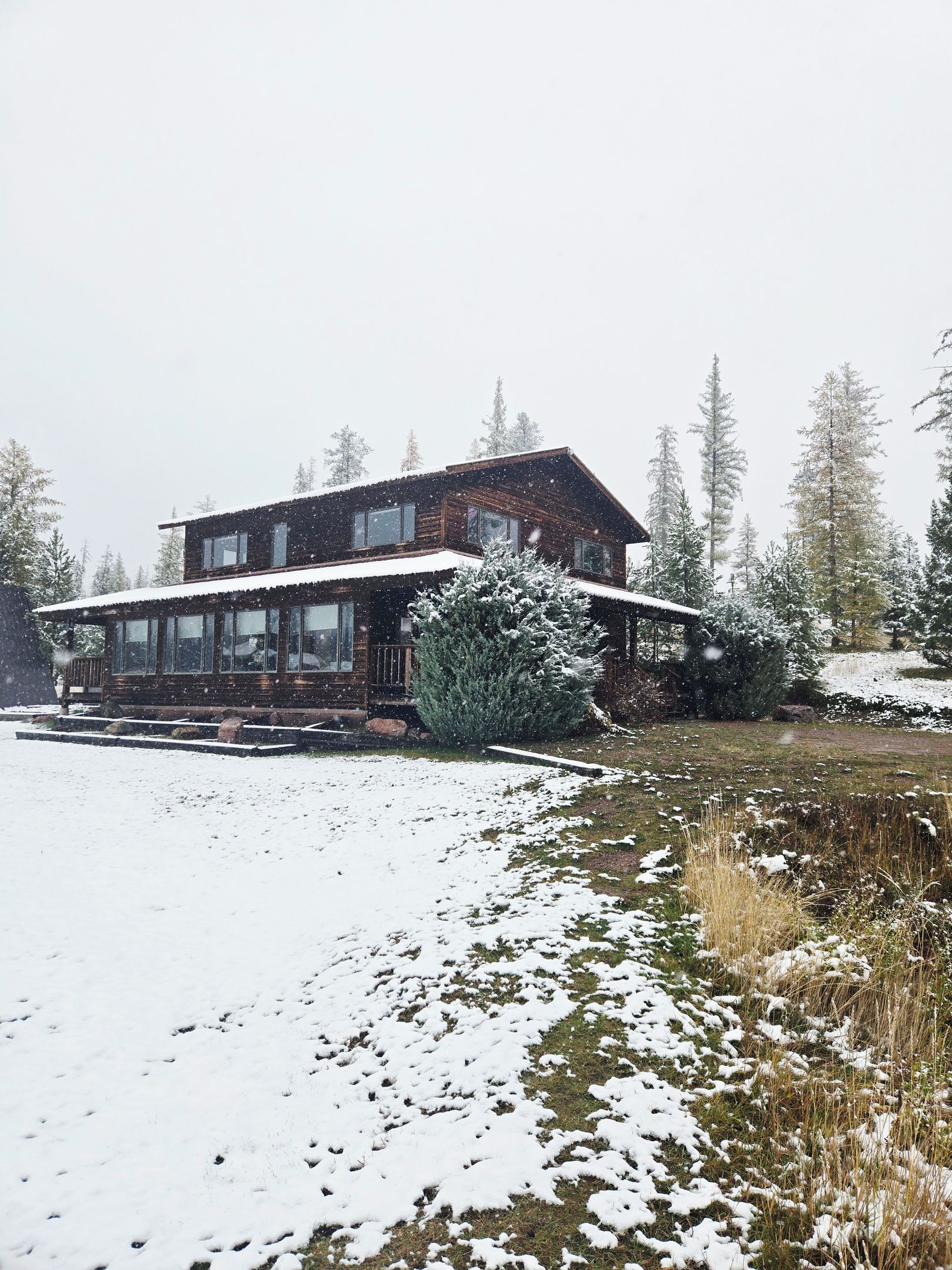 Eine Holzhütte mit einer breiten, fensterreichen Veranda, umgeben von schneebedeckten Bäumen.