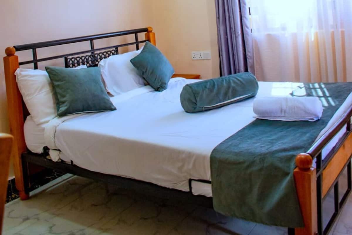 Un letto con struttura in legno, biancheria bianca e cuscini verdi.