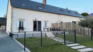 Ein zweistöckiges Haus mit geneigtem Dach, einem umzäunten Garten und einer gepflasterten Auffahrt.