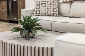 Ein modernes Wohnzimmer mit einem runden Couchtisch, einer Topfpflanze und einer Couch mit gemusterten Kissen.