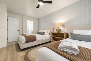 Ein Hotelzimmer mit zwei Betten, einem Deckenventilator, einer Nachttischlampe und einem gemusterten Wandpapier.