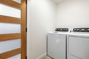 Ein Waschraum mit zwei weißen, von vorne befüllbaren Waschmaschinen und Trocknern, einer Holztür und einer weißen Wand.