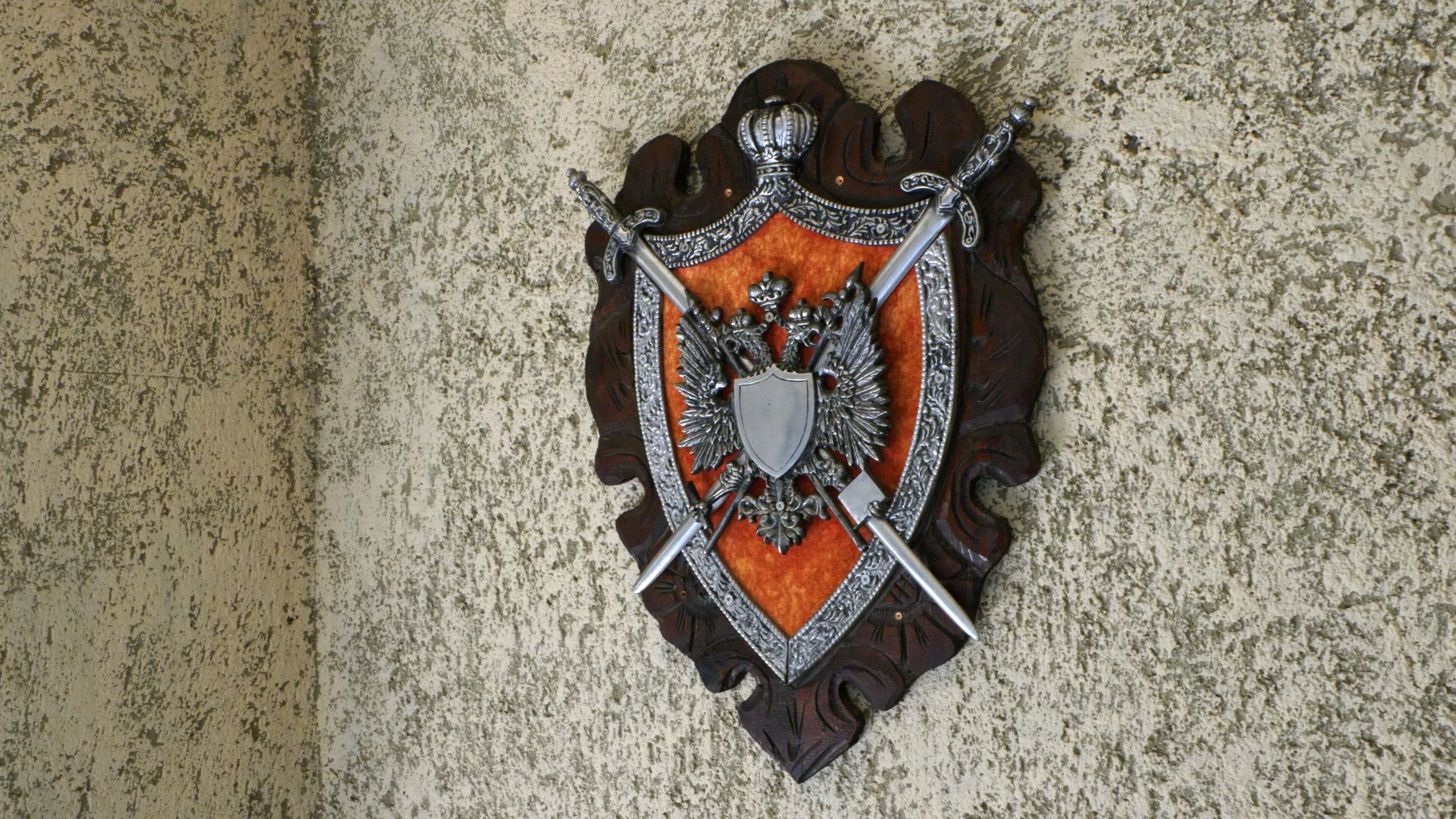 Seinälle kiinnitettävä koriste-embleemi, jossa on kilpi ja kaksi ristikkäin asetettua miekkaa.