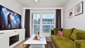 Un salon moderne doté d’un téléviseur à écran plat, d’un canapé vert, d’une table basse blanche et d’une grande fenêtre avec des rideaux.