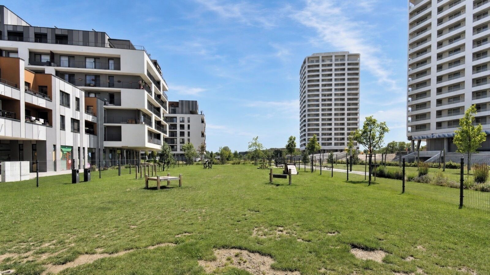 A grassy area with benches, surrounded by modern apartment buildings.