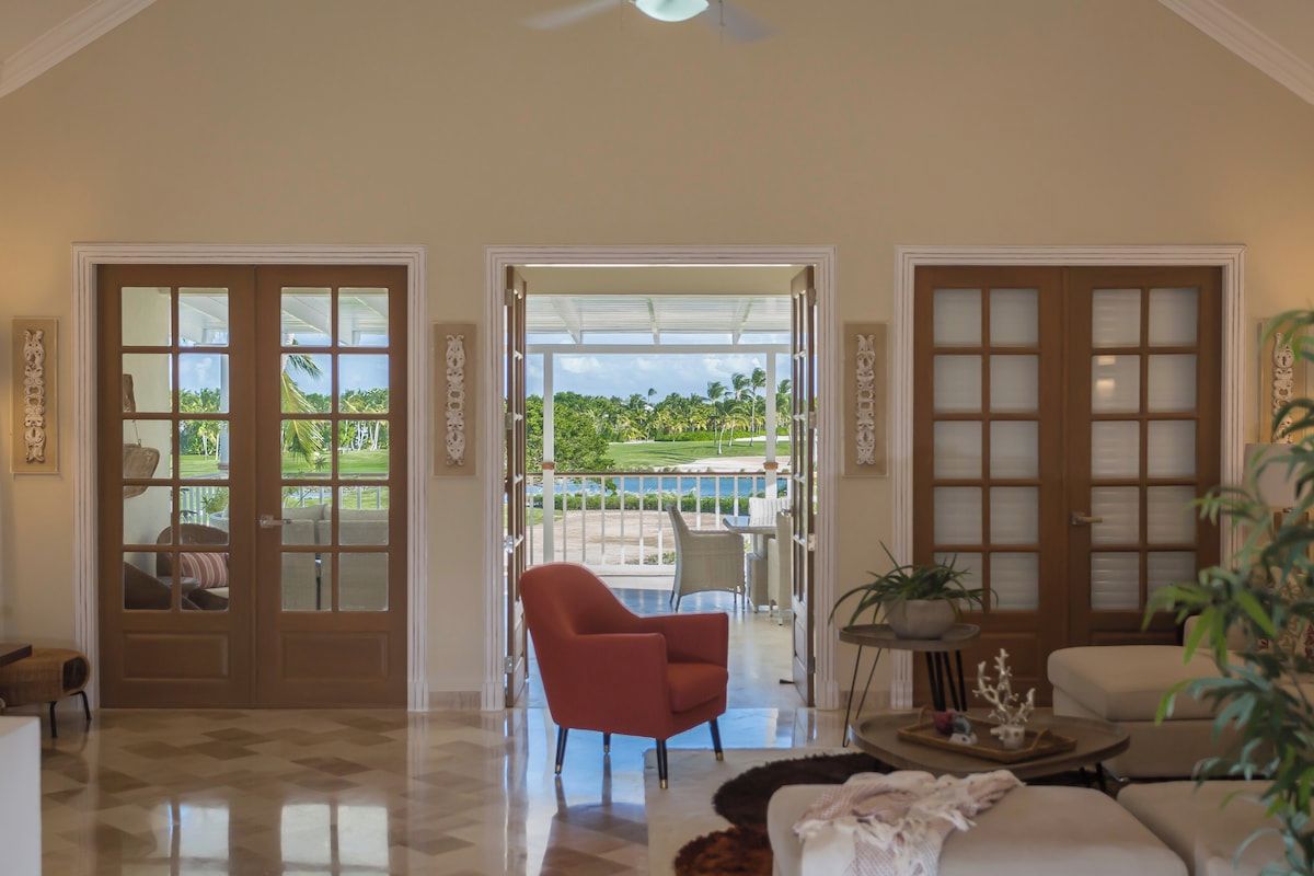 Sala de estar ampla com uma grande janela, uma poltrona vermelha e vista para uma piscina e áreas verdes.