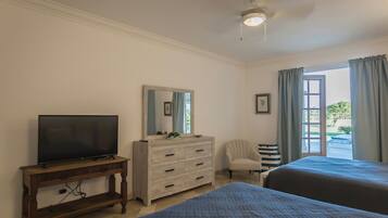 A hotel room with two beds, a TV on a wooden stand, a dresser, a chair, and a window with curtains.