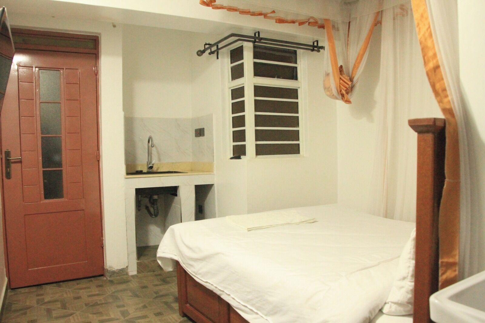 Quarto com cama, pia, janela com persianas e porta.