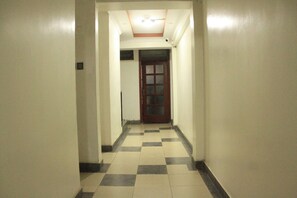 A narrow hallway with checkered flooring, a wooden door at the end, and a ceiling with recessed lighting. -  Exclusive Studios in Nairobi-kitchenette, WiFi, TV, fridge, microwave and more. (Nairobi)