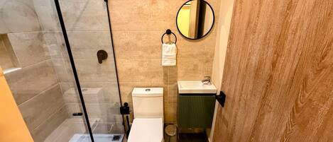 Un baño con cabina de ducha de vidrio, inodoro, lavabo y espejo.