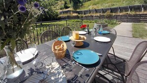 Un espace de restauration en plein air avec une table dressée pour deux personnes, entourée de chaises, d’un panier décoratif et d’un vase rempli de fleurs.