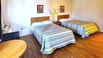 A hotel room with two beds, a wooden floor, a table, and a chair.