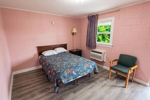 A bedroom with a bed, a nightstand, a chair, a window with curtains, and an air conditioning unit. - Hometown Inn Rocky Mount VA (Rocky Mount)