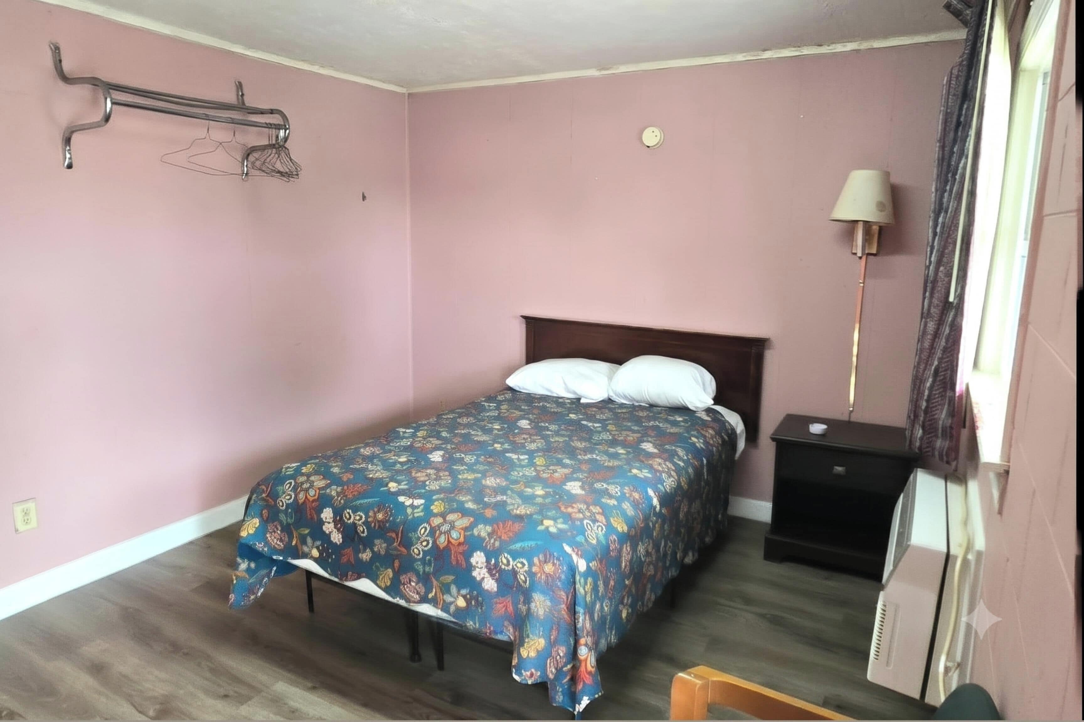 Un dormitorio con una cama, una mesita de noche, una lámpara y un estante en la pared.